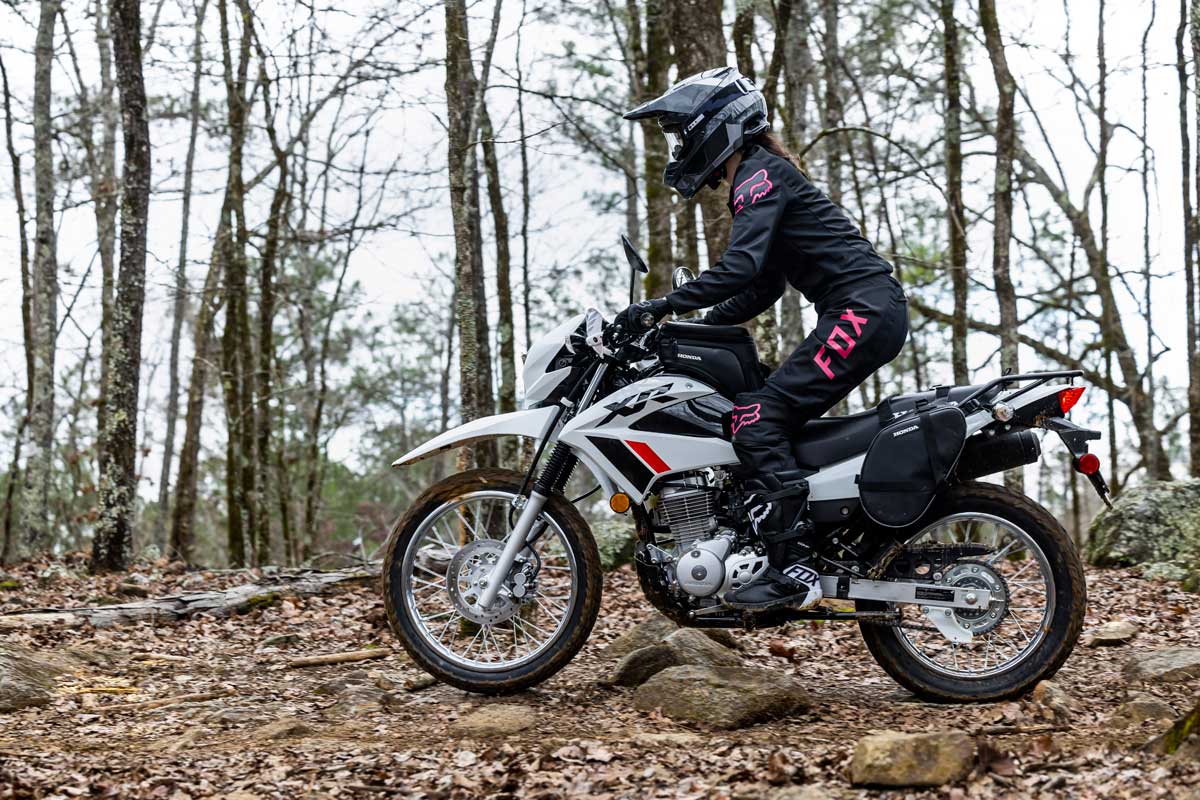 Rider on a lightweight dual-sport motorcycle navigating a dirt trail