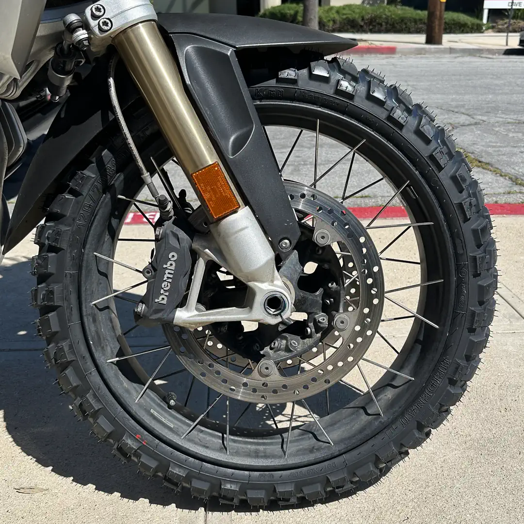 Hero image showing adventure motorcycle on gravel or dirt trail, tire detail visible