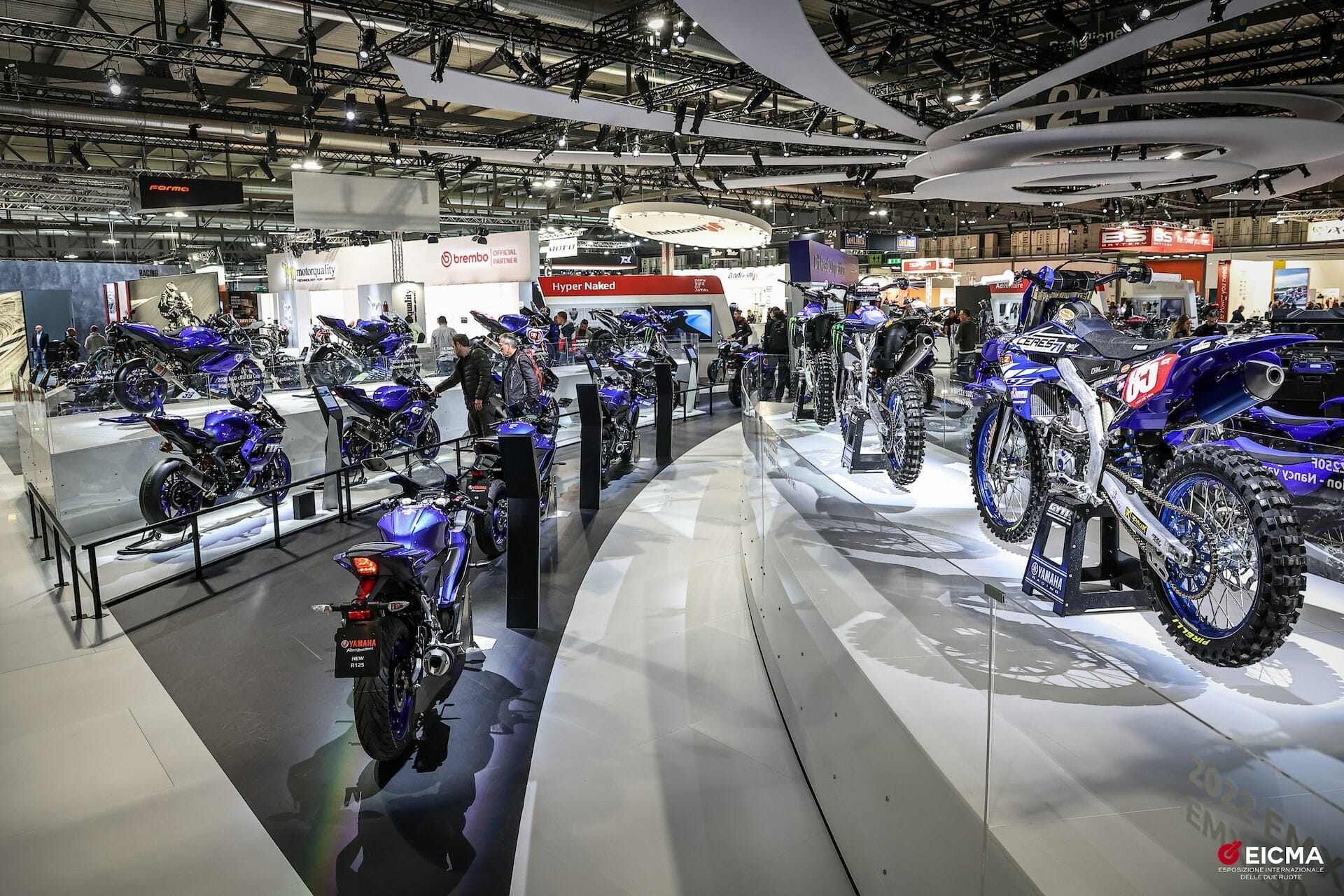 Hero image showing the EICMA show floor with motorcycles and crowds