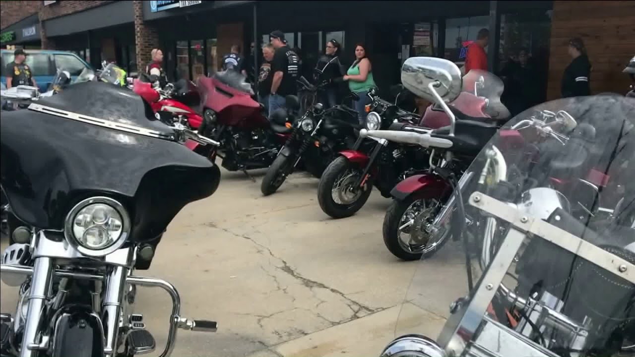 Motorcycle club meetup scene with riders socializing around bikes in a parking lot or venue