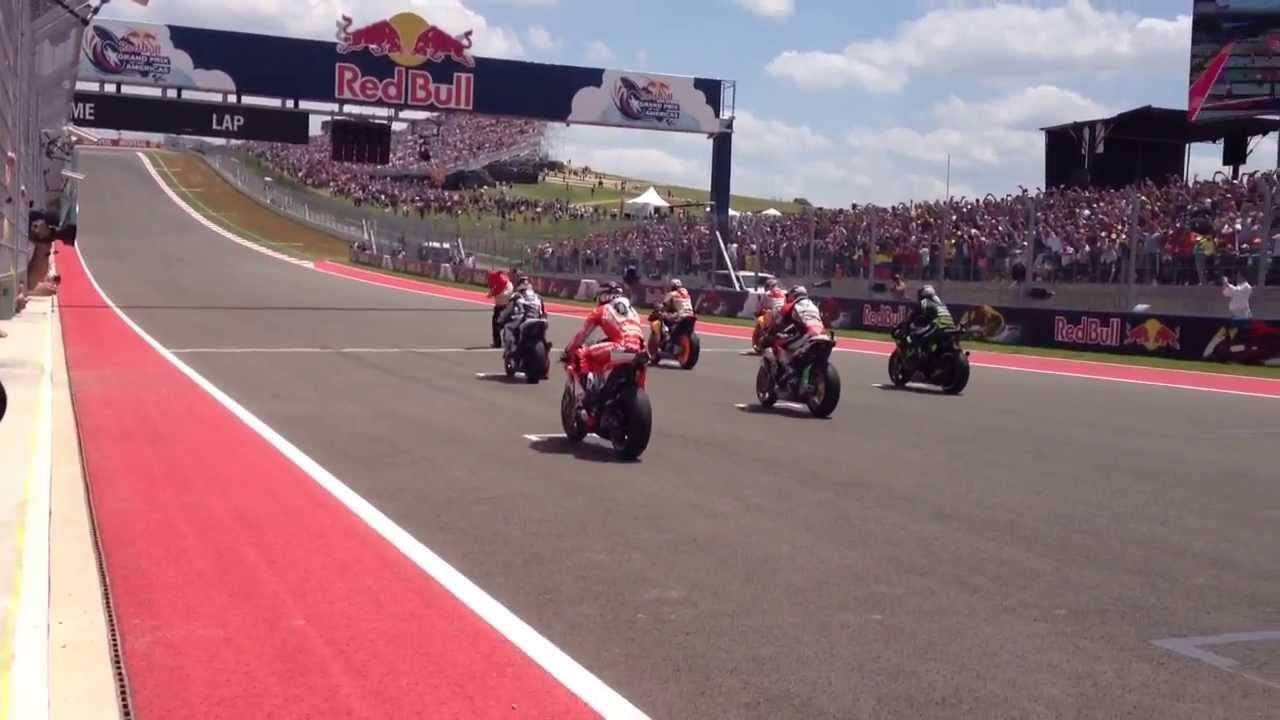 Race start action shot showing the full MotoGP grid launching off the line